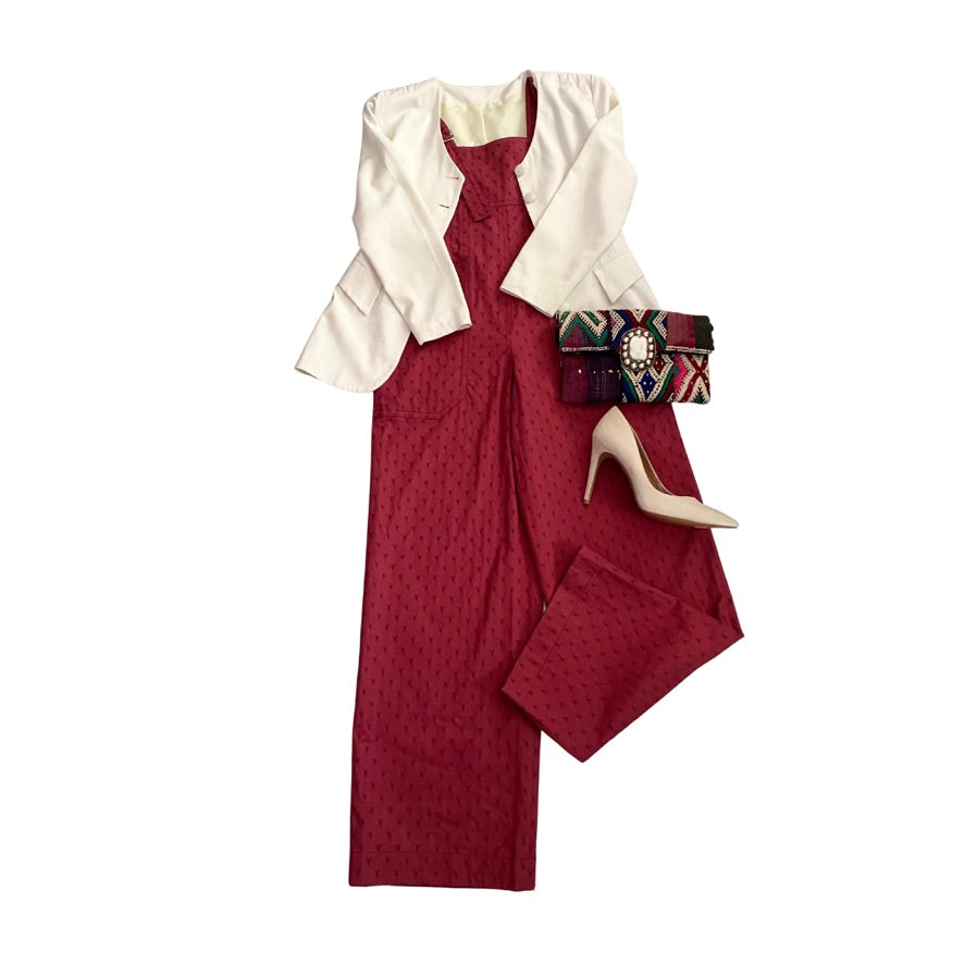 Red jumpsuit with cream jacket, clutch, and high heels on a white background