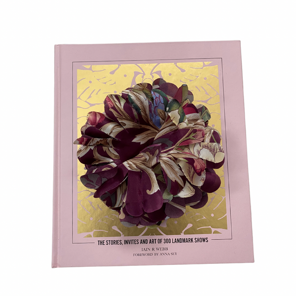Fabric flower brooch in plum and multicolour patterned fabric with layered petal design, placed on light wooden floor.