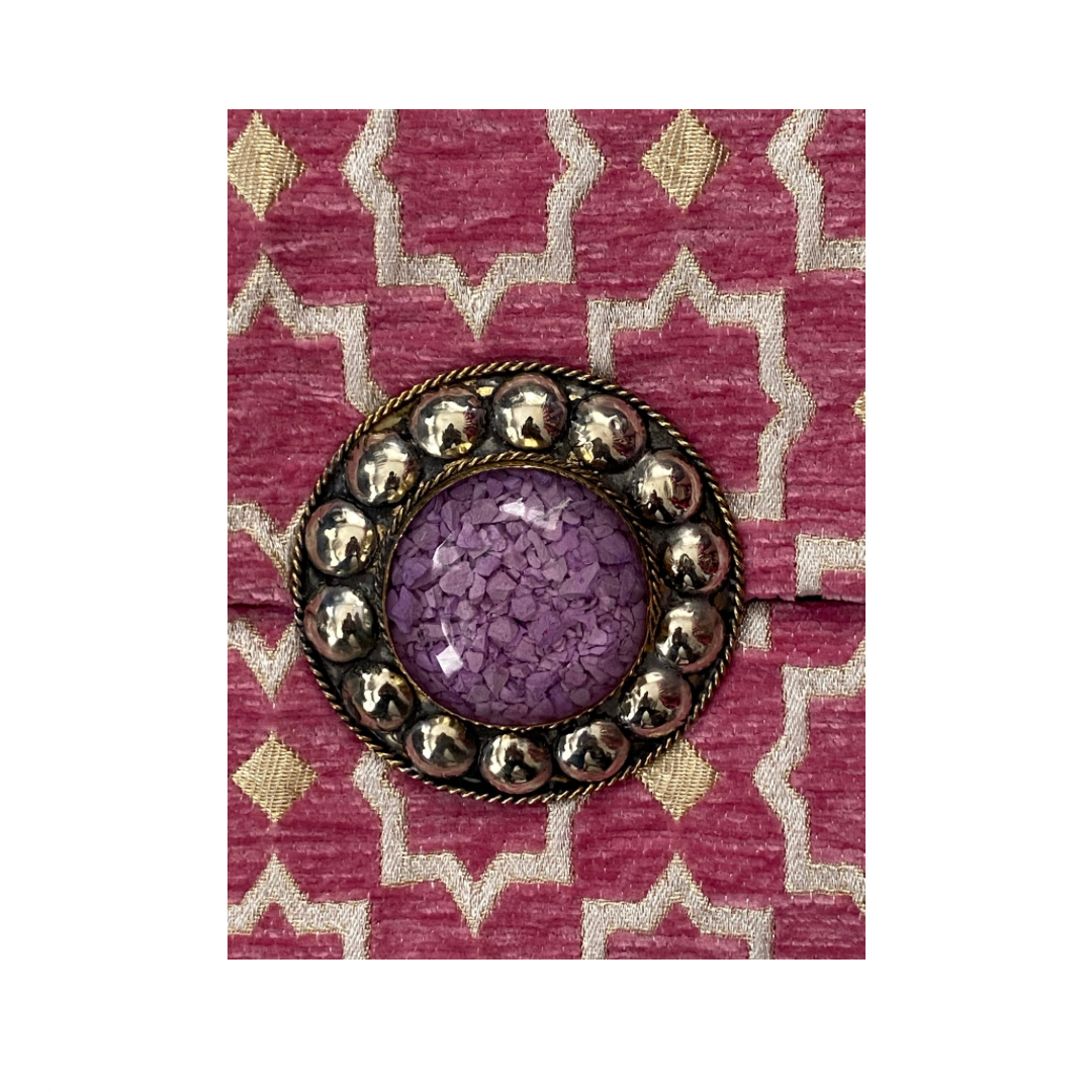 Decorative brooch with purple center and gold accents on a pink and white patterned fabric background