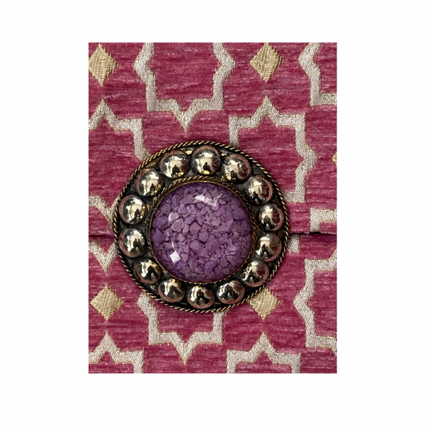 Decorative brooch with purple center and gold accents on a pink and white patterned fabric background