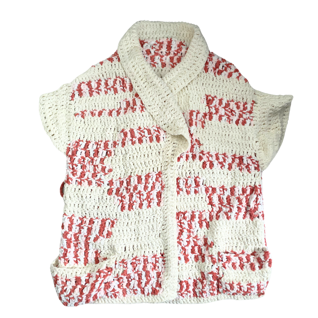 A chunky knit sleeveless cardigan in pink and cream colors with a shawl collar and deep front pockets.