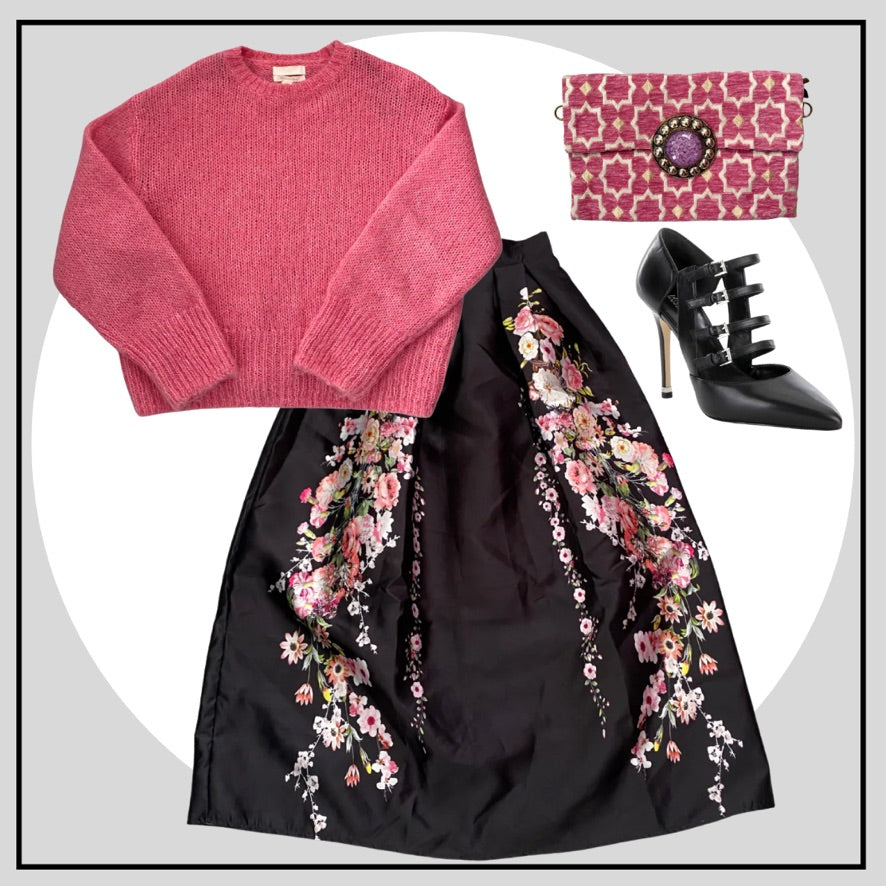 Pink sweater, black floral skirt, black high-heeled shoes, and pink clutch arranged on a white background.