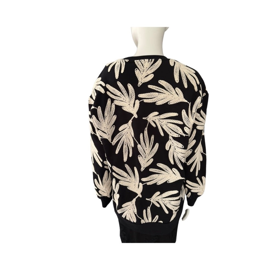 Black sweater with beige leaf pattern on a mannequin against a white background