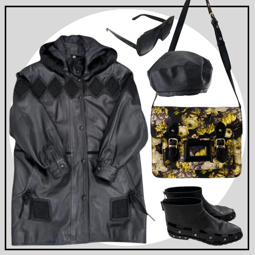 Black coat, sunglasses, beanie, floral bag, and black boots arranged on a light gray background.