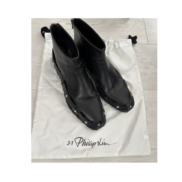 Black ankle boots on a branded white drawstring bag with '3.1 Phillip Lim' logo.