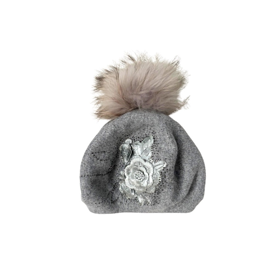 Grey knit beanie with floral embroidery and fur pom-pom on a white background