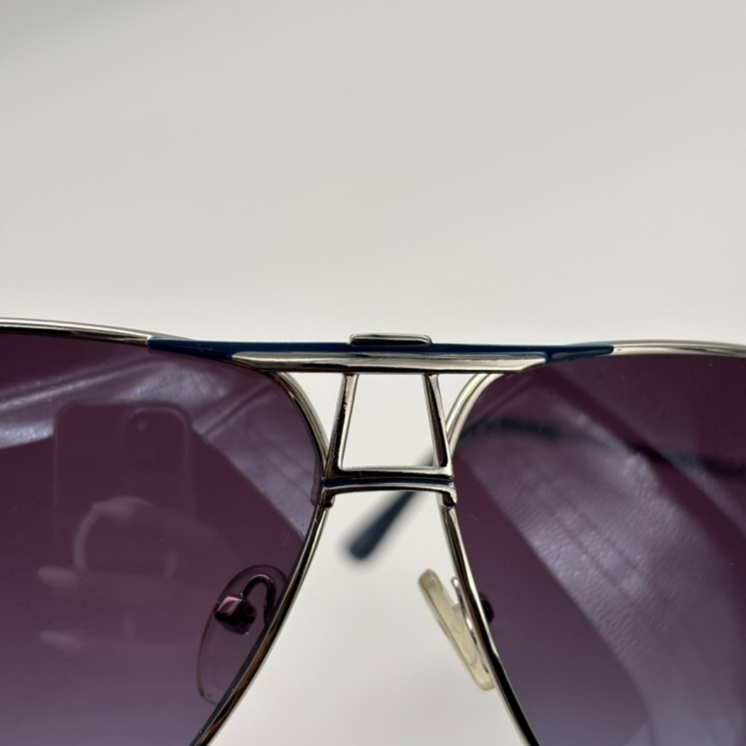 Close-up of a pair of sunglasses with purple lenses and gold frame on a light gray background