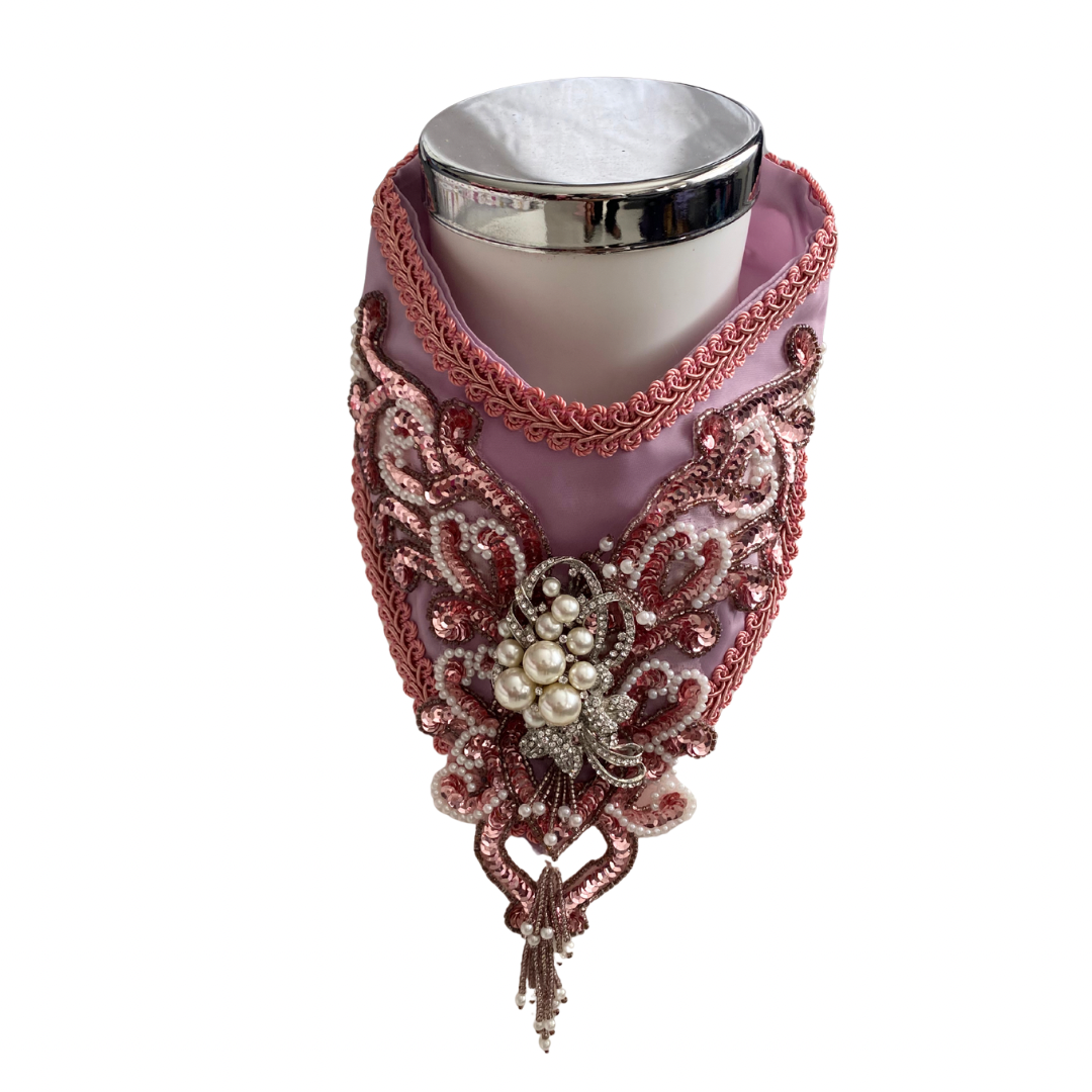 Decorative pink collar with intricate embellishment on mannequin neck on a white background