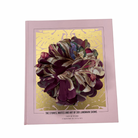 
Fabric flower brooch in plum and multicolour patterned fabric with layered petal design, placed on light wooden floor.