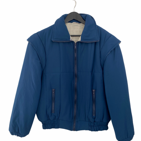 A vintage blue jacket with a cream check contrast collar lining, zip front fastening, and elasticated hem and cuffs. It features padded detailing and has a size XL label.