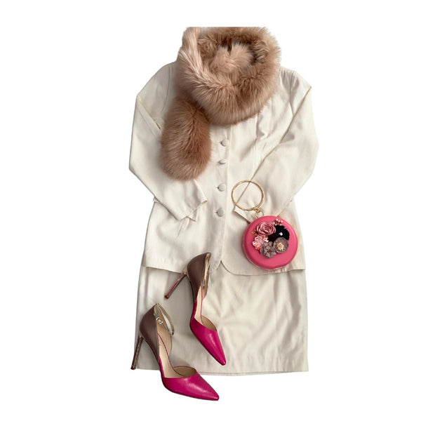Cream suit with fur stole, pink high heels, and pink handbag on a white background