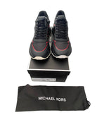 Black sneakers with red accents on a black box, accompanied by a Michael Kors pouch.