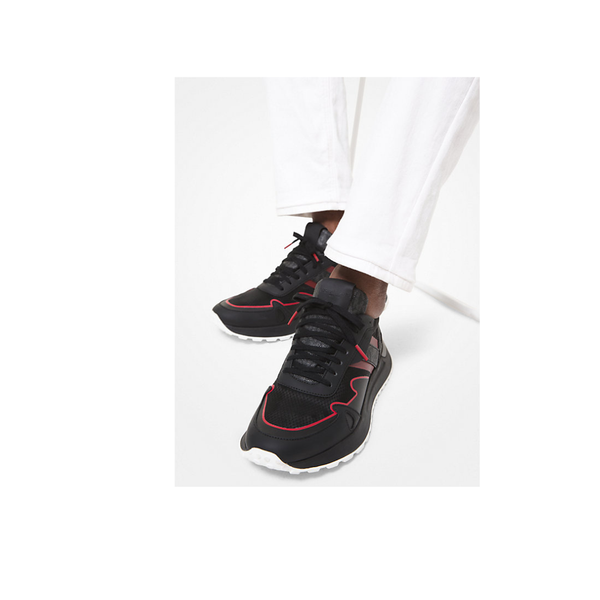 Black sneakers with red accents worn by a person on a white background