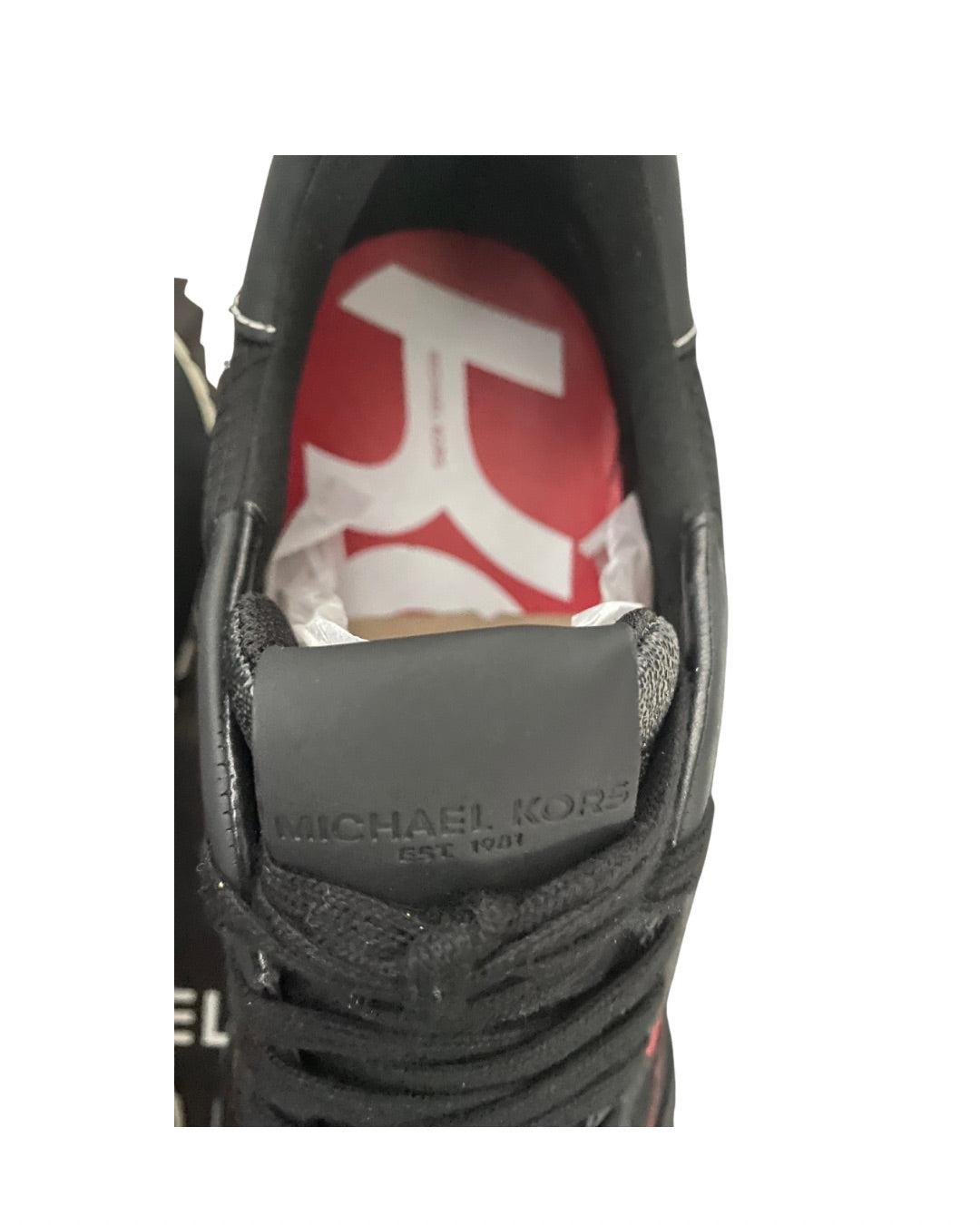 Close-up of a black Michael Kors shoe with a red and white logo on the tongue.