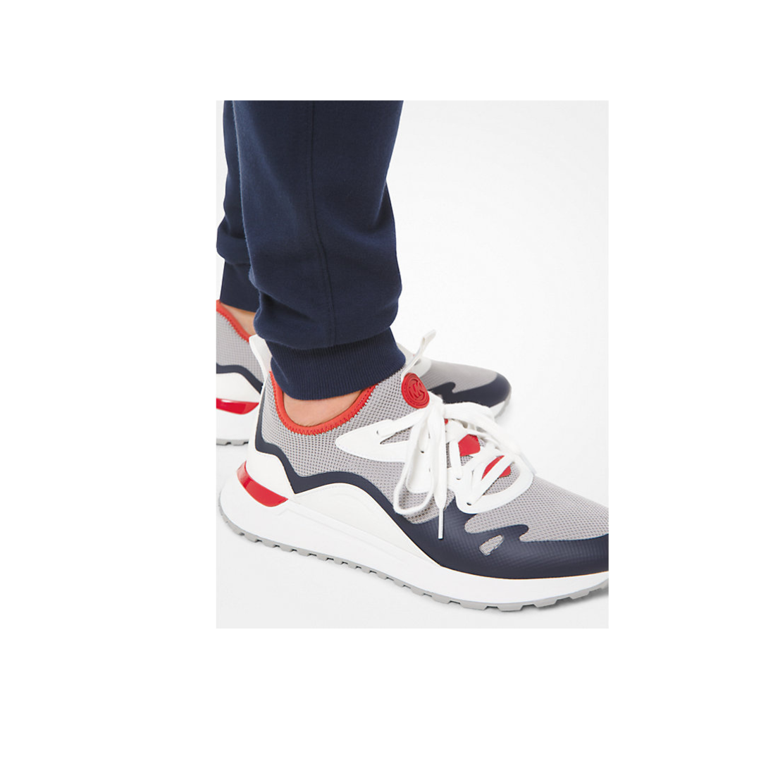 White sneakers with red and blue accents worn by a person in navy pants on a white background