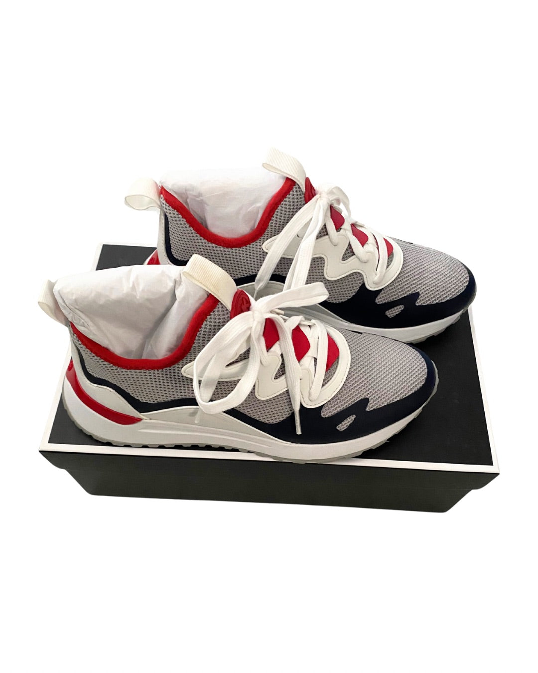 Gray sneakers with red and white accents on a black box against a white background