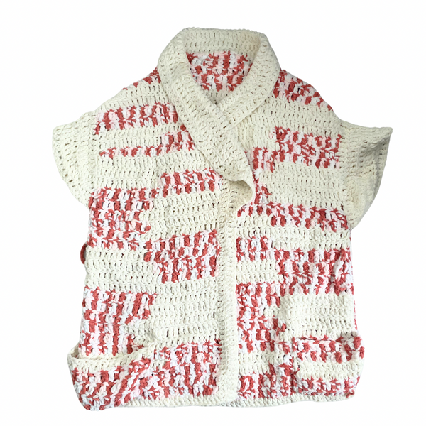 A chunky knit sleeveless cardigan in pink and cream colors with a shawl collar and deep front pockets.