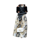 Woman wearing a floral skirt, black top, and white gloves with a white handbag on a white background