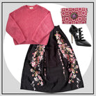 Pink sweater, black floral skirt, black high-heeled shoes, and pink clutch arranged on a white background.
