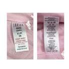 Two clothing labels on a pink fabric background, one showing size and care instructions, the other showing color information.