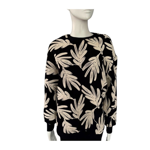 Black sweater with beige leaf pattern on a mannequin against a white background