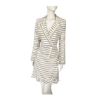 A cream colored tweed skirt suit with horizontal stripes, structured blazer and ruffle detailing, displayed on a mannequin.