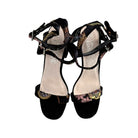 Black high-heeled sandals with floral design on a white background