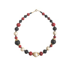 A vintage necklace featuring a combination of deep ruby red, onyx black, and soft ivory-hued faux pearls with gold-tone hardware.