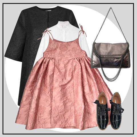 Pink dress with black top, black shoes, and silver handbag on a light gray background