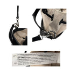 Close-up of a beige bag with black strap and metal clasp, featuring a label with text.