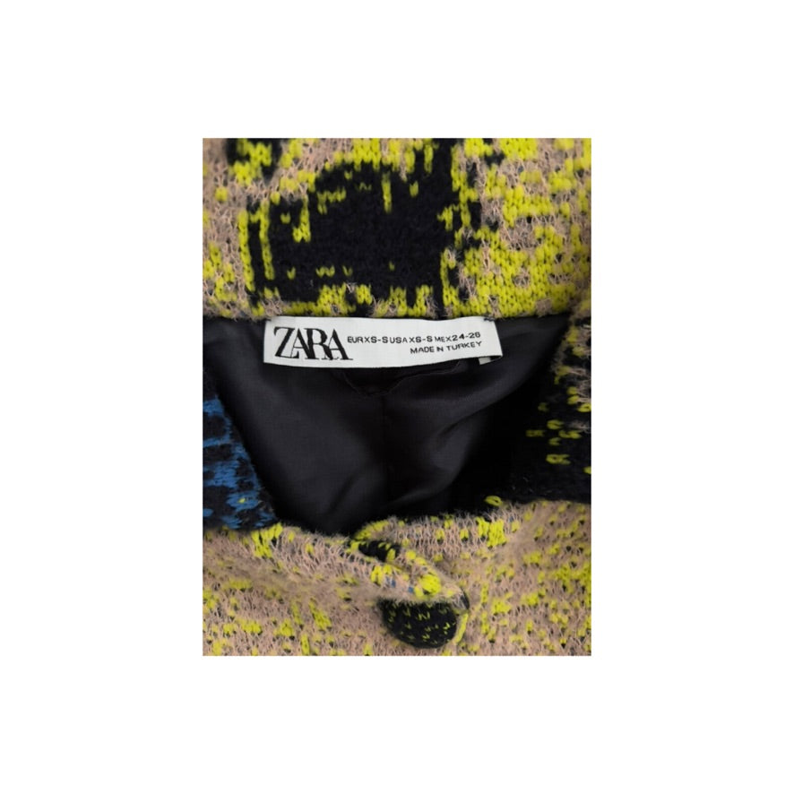 Close-up of a Zara label on a multicolored fabric with black and yellow patterns.