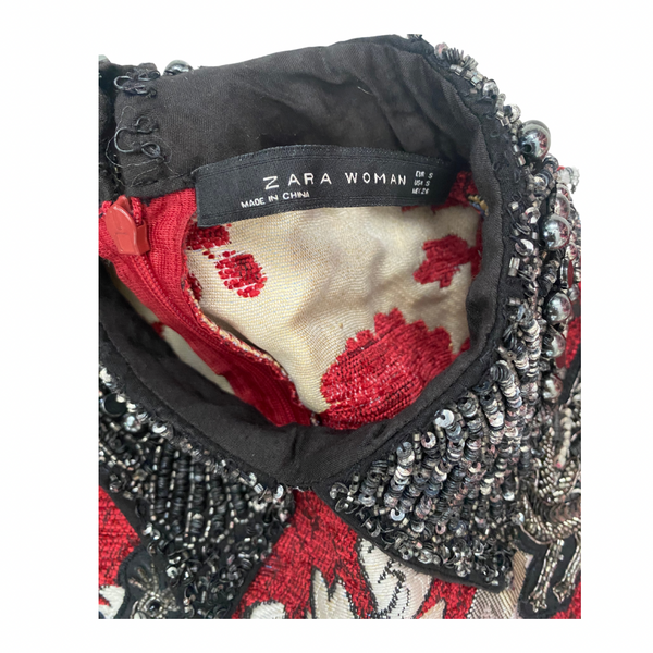 Close-up of a Zara Woman label on an embroidered garment with red and black patterns.