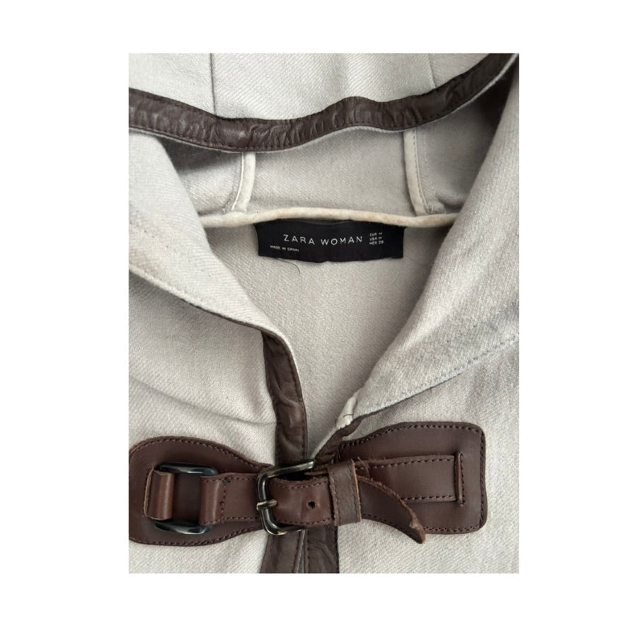 Close-up of a Zara Woman coat with a brown belt and visible label.